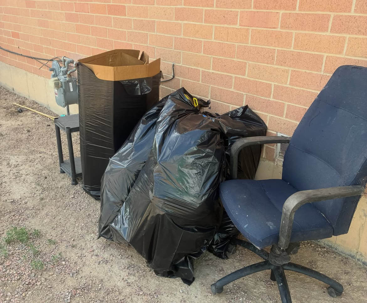 Bagged trash, an old office chair, and a cabinet piled outside a commercial building before pickup